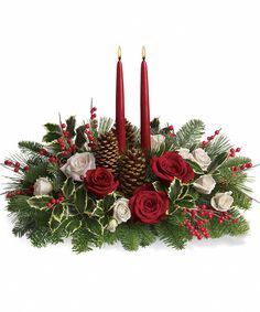 a christmas centerpiece with two candles and evergreens in the center, surrounded by red roses