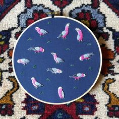 a close up of a embroidery on a rug with birds in pink and blue colors