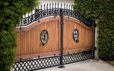 an iron and wood gate in front of a house with green bushes on either side