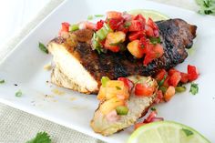 two pieces of meat on a white plate with tomatoes and green garnishes