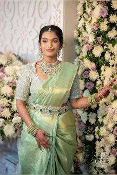 a woman in a green and white sari posing for the camera with flowers behind her