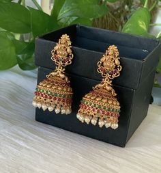 a pair of gold toned earrings with multicolored stones and pearls hanging from them