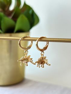 DESCRIPTION: Dainty gold huggie hoops with gold stegosaurus dinosaur charms Dainty Dinos for everyday wear! MATERIALS: Hoops and Charm- 24K Gold Plated Nickel & Lead Free ♡ MEASUREMENTS: Hoop - 13mm Charm - 12mm drop PACKAGING: Each order is packaged in a pink jewelry bag and white box- perfect for gifting! FREE SHIPPING for orders of $35+ LET'S STAY CONNECTED! www.instagram.com/NYCelestialCo Gold Novelty Drop Earrings, Novelty Gold Hypoallergenic Earrings, Gold Hypoallergenic Novelty Earrings, Hoop Earrings With Charm, Dinosaur Jewelry, Dinosaur Earrings, Small Gold Hoops, Earrings Hoop, Pink Jewelry