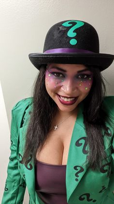 a woman wearing a green jacket and hat with question marks painted on it's face