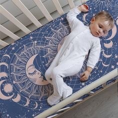 a baby laying in a crib with the moon and stars on it's side