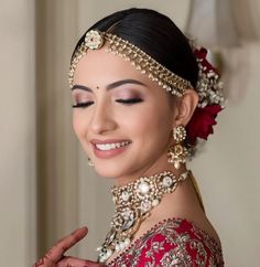 a woman in a red and gold bridal outfit smiles at the camera while holding her hands together