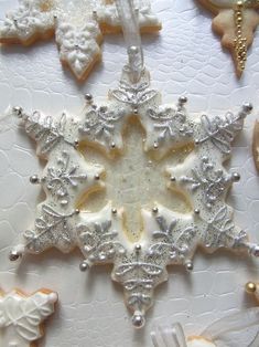 some white and gold decorated cookies are on a tablecloth with silver ornaments hanging from it