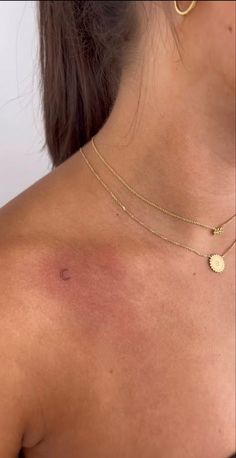 the back of a woman's neck with a small gold disc pendant on it