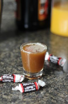 a shot glass filled with caramel flavored candy on a counter top next to two bottles of orange juice