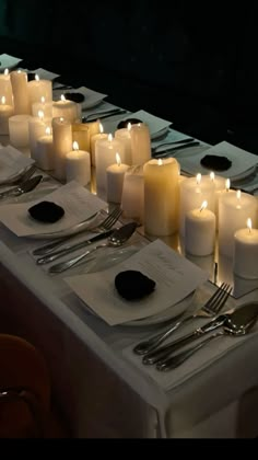 many lit candles are set on a long table with silverware and napkins in front of them