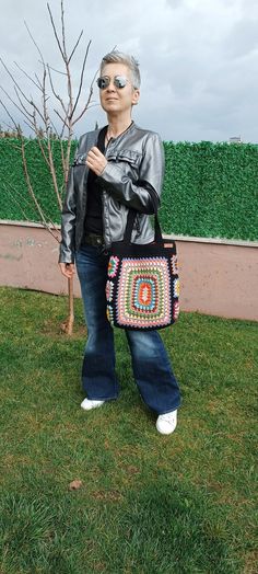 a woman standing in the grass holding a purse