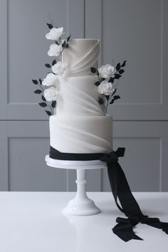 a white wedding cake with black ribbon and flowers