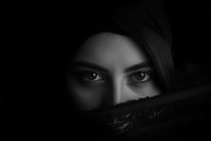 a woman's face peeking out from behind a dark cloth with her eyes wide open