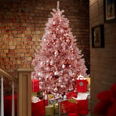 a pink christmas tree with presents under it in front of a brick wall and stairs