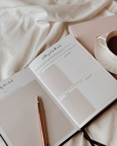 an open book and pen sitting on top of a bed next to a cup of coffee