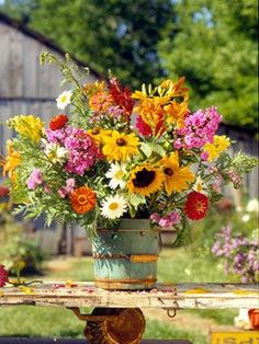 a vase filled with lots of flowers sitting on top of a wooden table in the middle of a yard