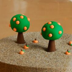 three small green trees with orange polka dots on them sitting in the middle of sand