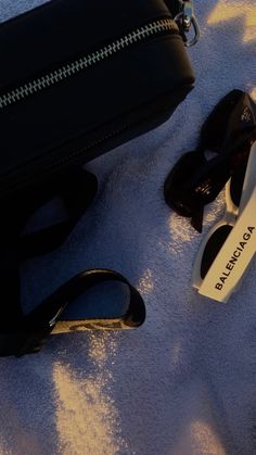 two pairs of black and white sunglasses laying next to a purse on a blue blanket