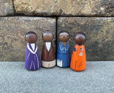 three wooden figurines are standing next to each other on the sidewalk in front of a stone wall