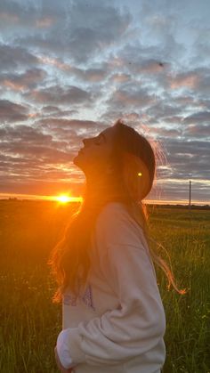 a girl is standing in the grass with her head turned to the side, looking up at the sky