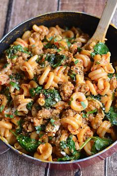 a skillet filled with pasta, meat and spinach on top of a wooden table