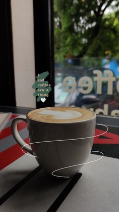 a cappuccino coffee cup sitting on top of a table next to a window