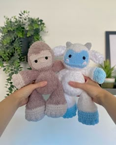 two stuffed animals are being held by someone's hands in front of a potted plant