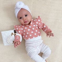 a baby laying on top of a white blanket next to a handbag and purse