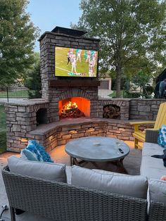 an outdoor fireplace with seating around it and a flat screen tv on the back wall