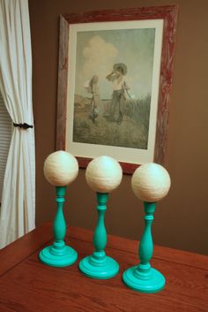 three blue lamps sitting on top of a wooden table next to a framed painting and window