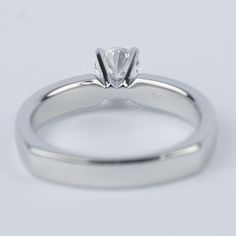 a white gold engagement ring with a single diamond in the center, on a plain surface