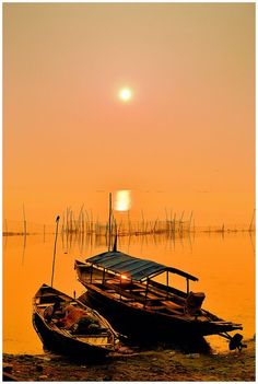 two boats are sitting in the water at sunset