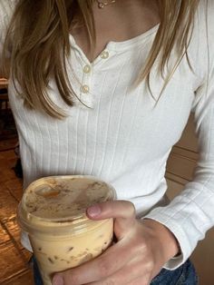 a woman is holding a jar of food in her hands and wearing a white shirt