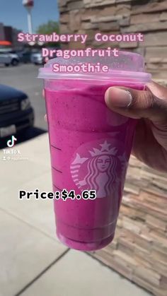 a person holding up a pink drink in front of a building with the words strawberry coconut dragonfruit smoothie on it