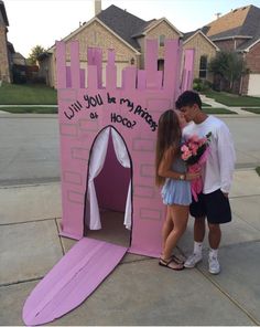 a man and woman standing in front of a pink castle with writing on the door