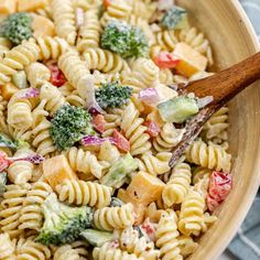 a pasta salad with broccoli, tomatoes and cheese in a wooden serving bowl