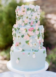 a three tiered cake decorated with pink and blue flowers on a white table outside