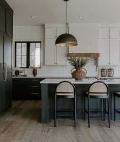 a kitchen with white cabinets and black countertops, two chairs at the center island