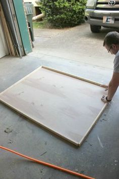 a man is working on an unfinished piece of wood in front of a garage door