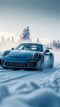 a blue sports car driving down a snow covered road with trees in the back ground