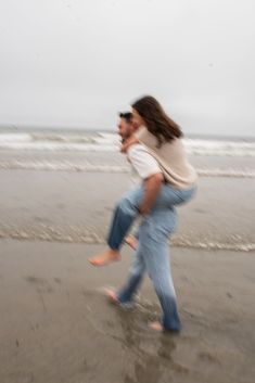 a man carrying a woman on his back while walking along the beach in front of the ocean