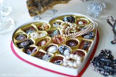 a heart shaped box filled with lots of different types of buttons and pearls on a table