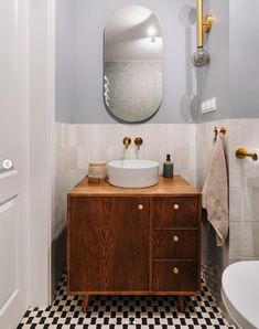 a bathroom with black and white checkered flooring, a round mirror above the sink