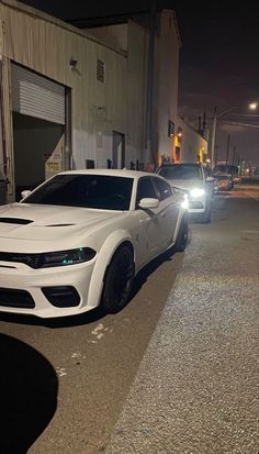 the white car is parked on the side of the road near other cars at night