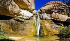 a man standing at the base of a waterfall in front of some large rock formations