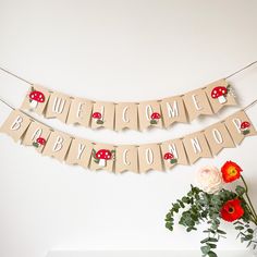 a welcome baby banner hanging on a wall next to a vase with flowers and greenery