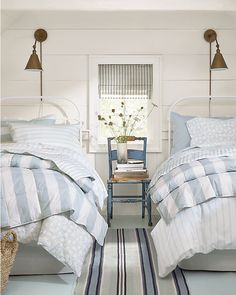 two beds with blue and white comforters in a bedroom next to a chair, rug and window