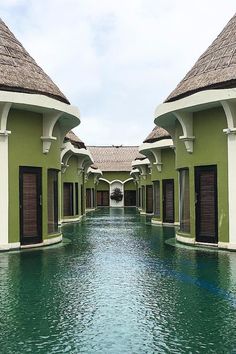 an outdoor swimming pool with thatched roofs and shutters on each side, surrounded by water