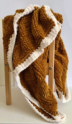 a brown and white knitted blanket sitting on top of a wooden chair next to a wall