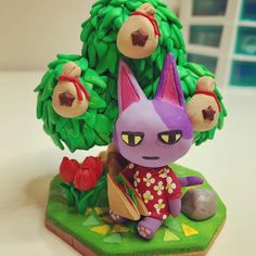 a figurine of a cat sitting next to a tree with flowers on it